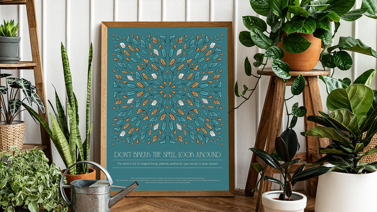 art print frame sitting on the floor of a room, plenty of plants around, poster of leaves and crystals mirrored like a kaleidoscope and shaped like a tile with text under, titled "don't break the spell, look around""