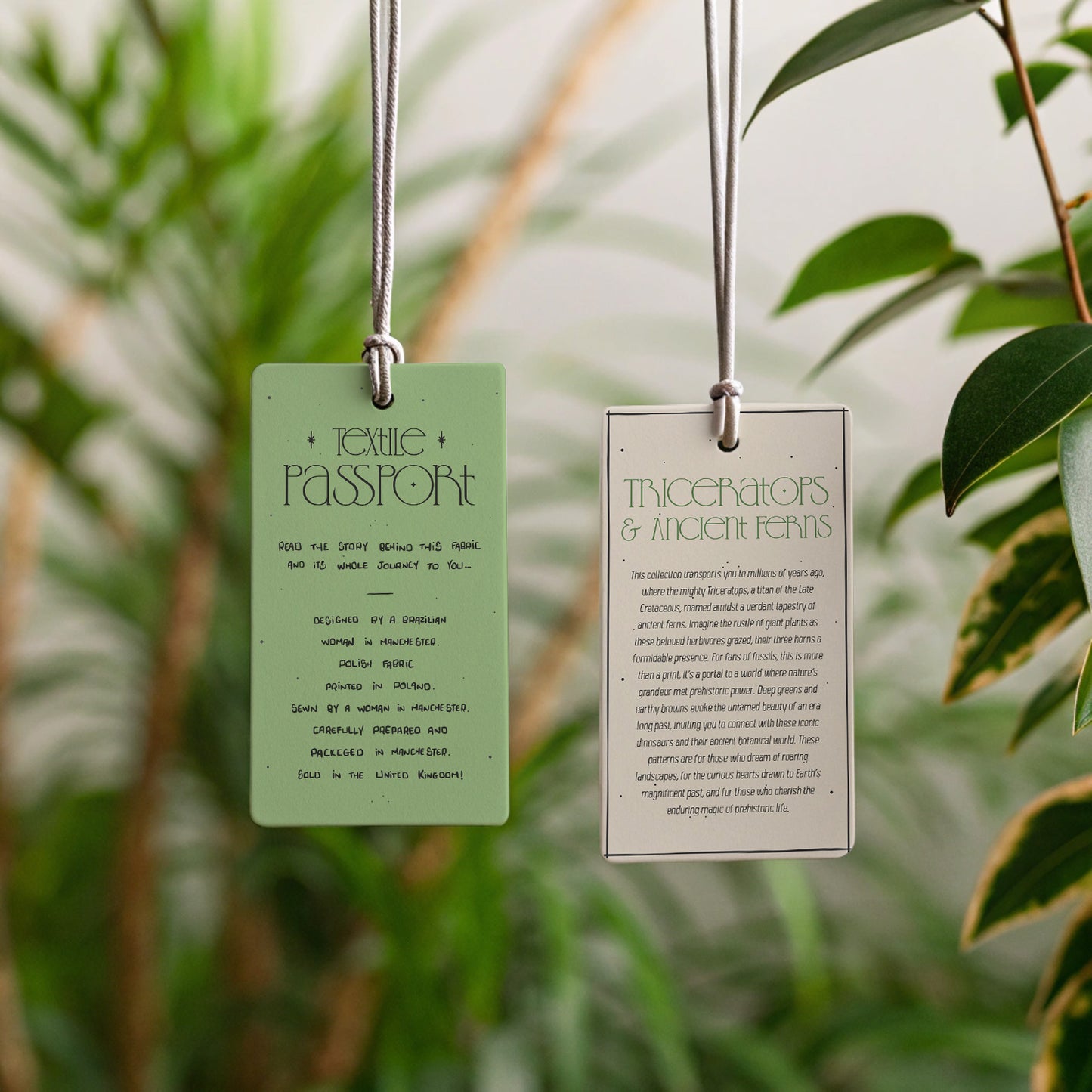 Two hanging tags with text against a blurred green leafy background; triceratops & ancient ferns collection bio; textile passport