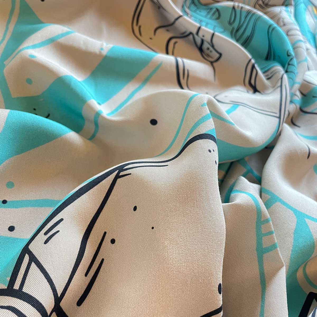 Close up of printed fabric, crinkled fabric on table, zoom in on material, cream, bright turquoise and black outline of plants illustrations