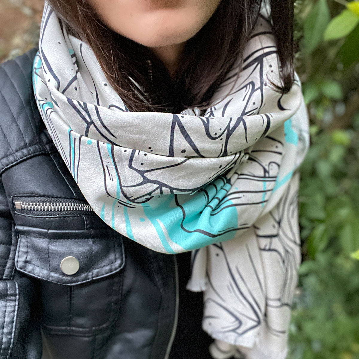 Woman wearing scarf wrapped around neck, black leather jacket outfit, special design printed fabric in cream, turquoise and black outlines, rock and roll look.