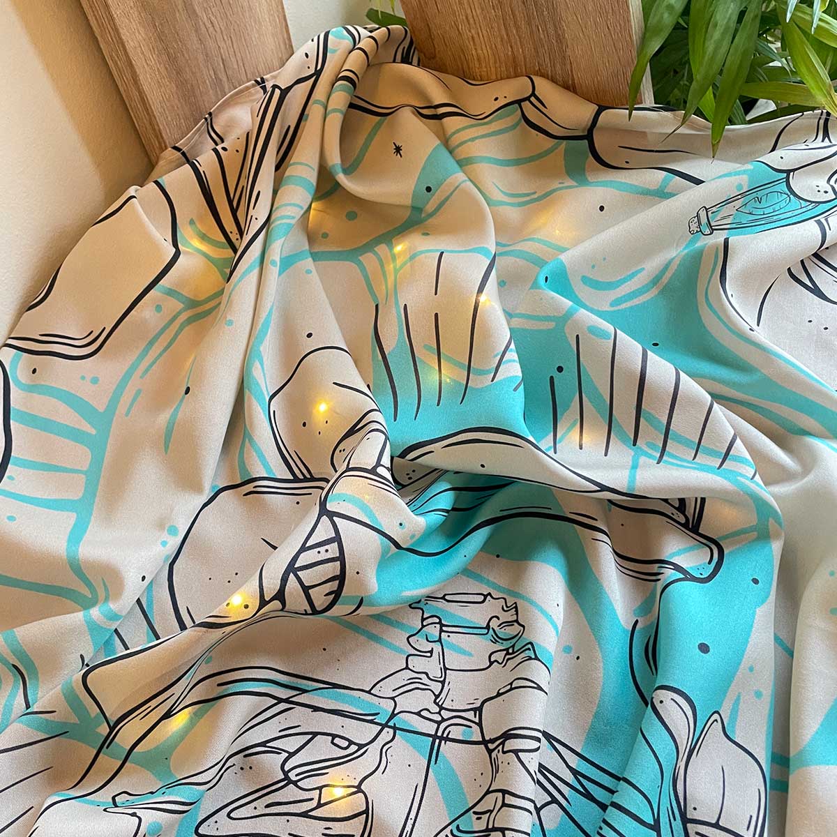 Fabric laid on table, palm leaves next, sunlit room. Illustration of skeleton inside huge glass jar and heavy tropical jungle on the border of fabric. Fabric sewn on hems