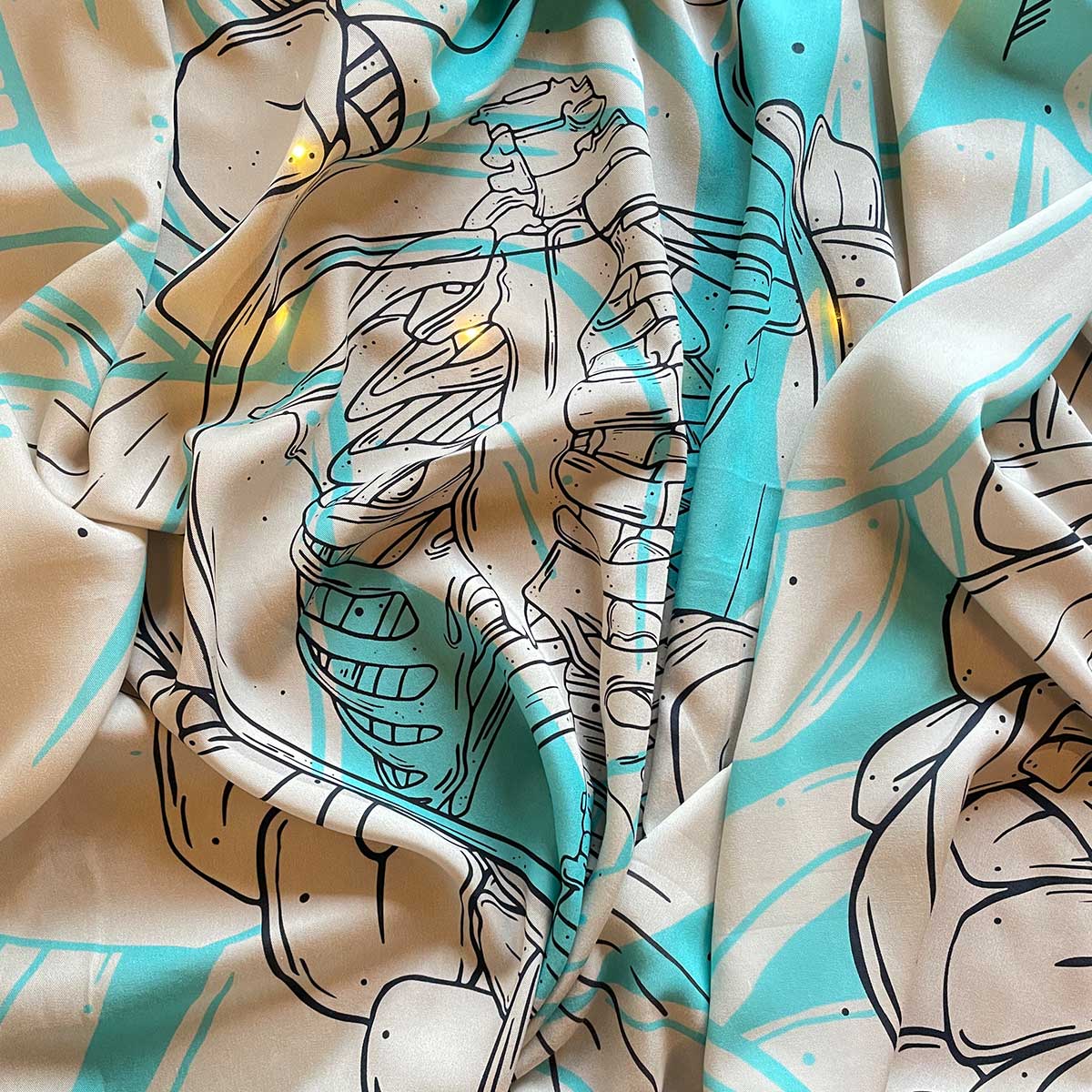 Top view of fabric in cream, bright turquoise and black outlined illustration of huge skeleton inside glass jar, fairy lights under, crinkled fabric.