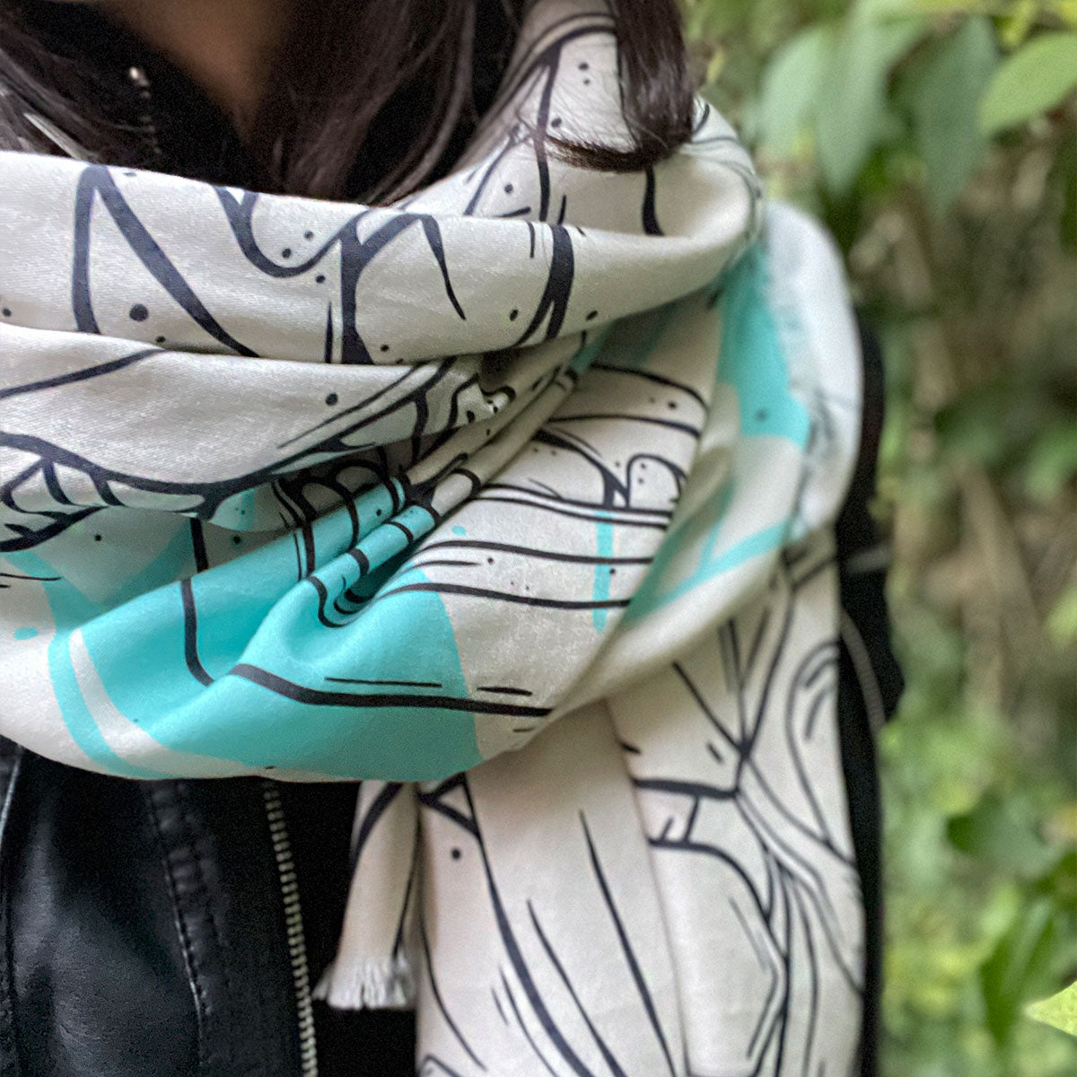 Woman wearing scarf wrapped around neck, black leather jacket outfit, special design printed fabric in cream, turquoise and black outlines.
