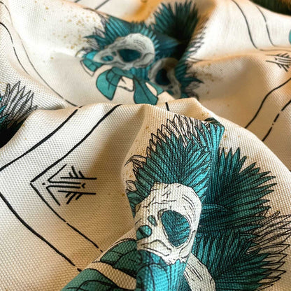 Close up of tea towel wrinkled fabric. Tropical leaves in teal with bird skull design, runes and lines in black, all over pattern