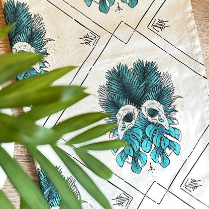 Tea towel open top view. Tropical leaves in teal with bird skull design, runes and lines in black, all over pattern