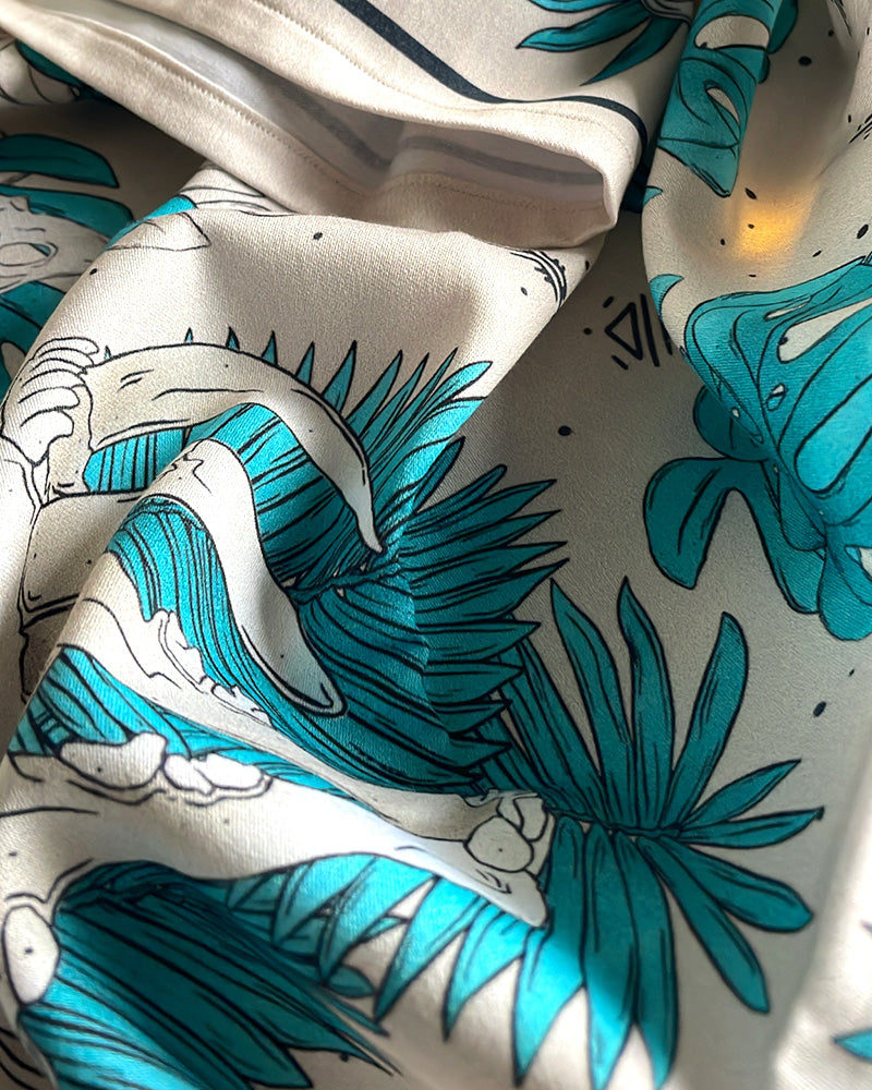 A close-up of draped fabric featuring a tropical print with turquoise palm leaves, rune icons and saber tooth tiger skull. exotic prints on bandanas