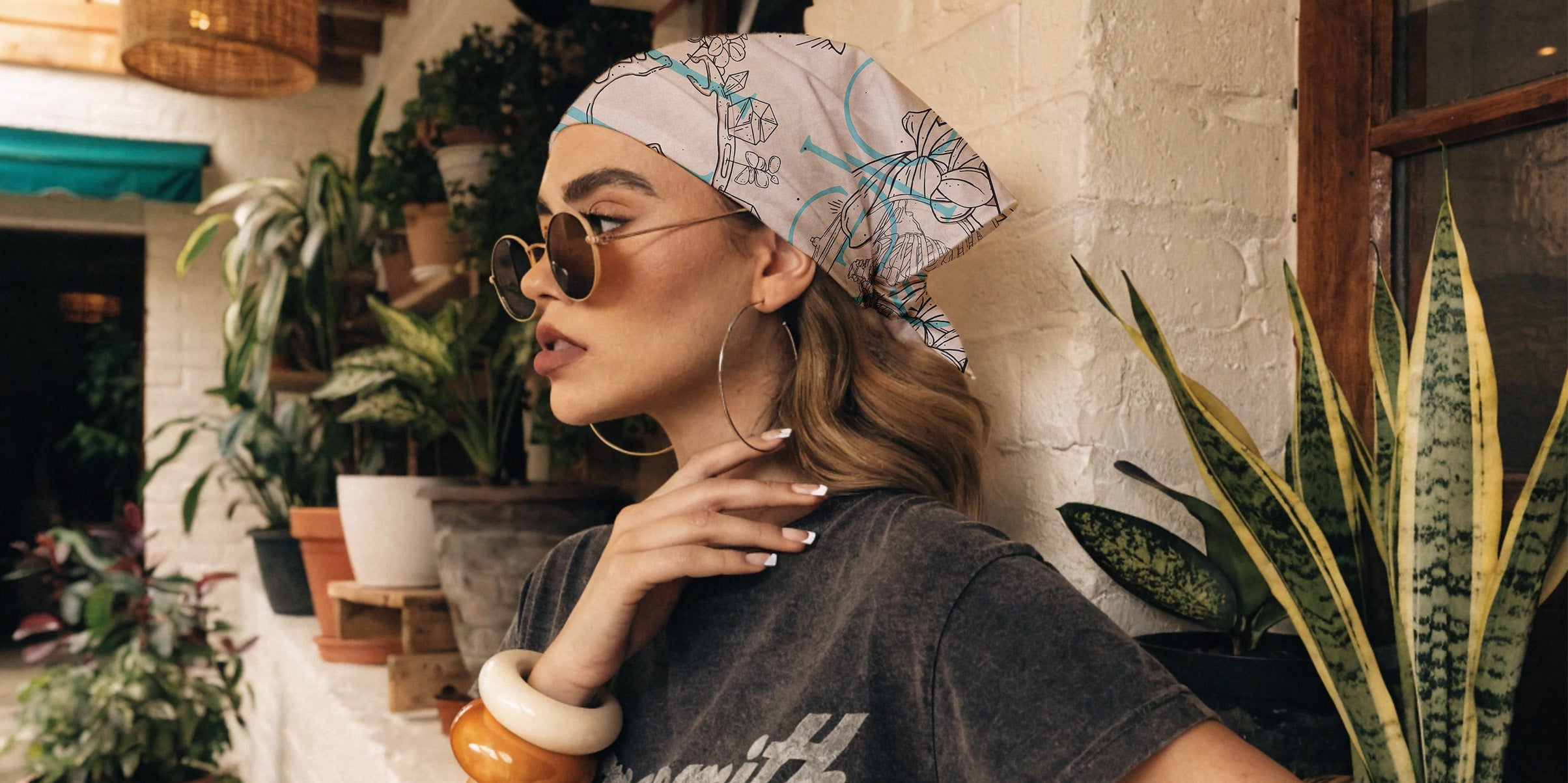 young woman posing wearing head scarf, boho bandana, hair accessory, round sun glasses, plants surround the scene