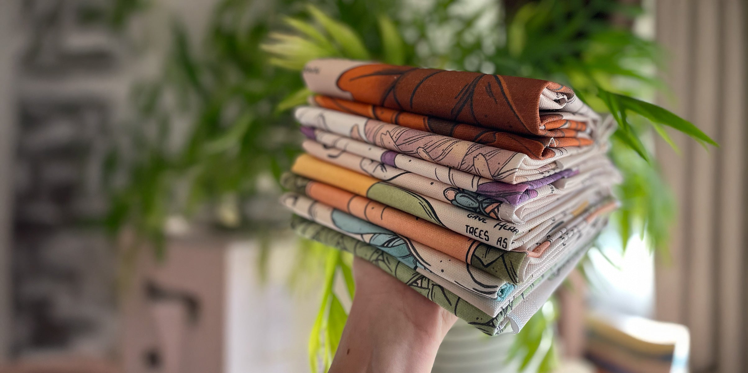 illustrated tea towels with text, campfield market, printed textiles folded stacked up on a pile, hand holding it up