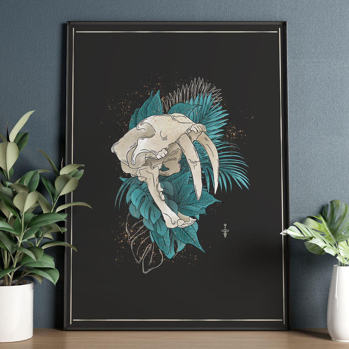 Photo of art print framed sitting on wooden table, plants surround it. Bold design of big sabertooth skull with loads of teal tropical forest leaves. Dark background and tiny rune. 