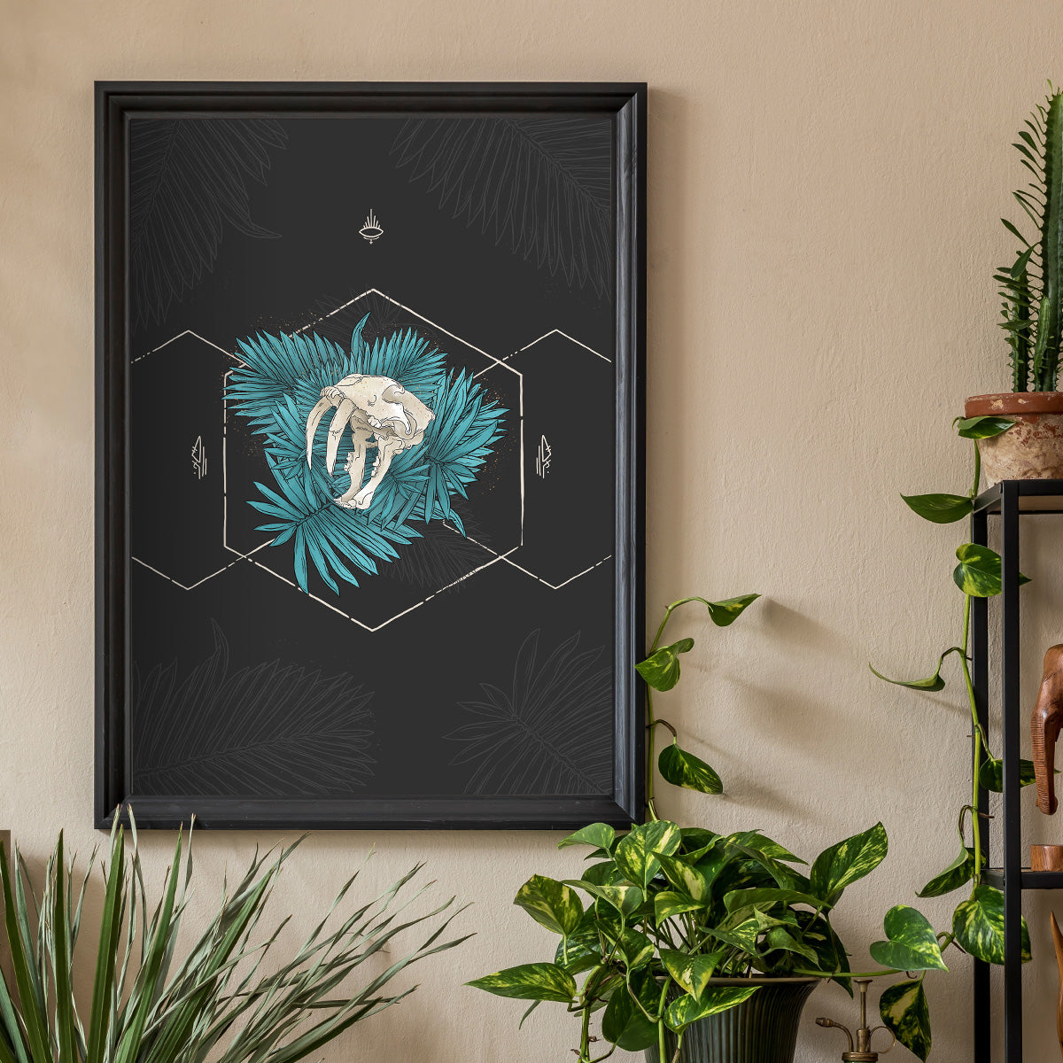 Art print framed hanged, plants surround it, design shows outlined hexagons cream lines, leaves inside with sabertooth skull showing teeth in the centre. Dark grey background