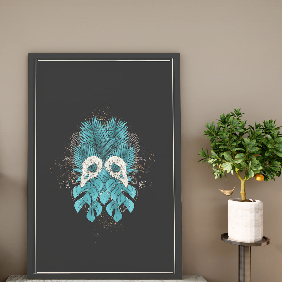 art print sitting on shelf, design of two bird skulls mirrored, bold tropical forest leaves in teal, charcoal background